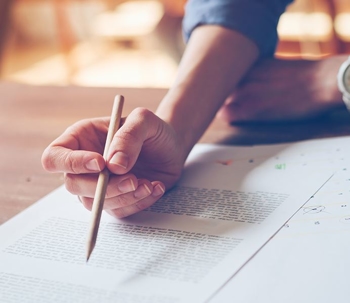 Hand holding pencil writing on sheet of paper